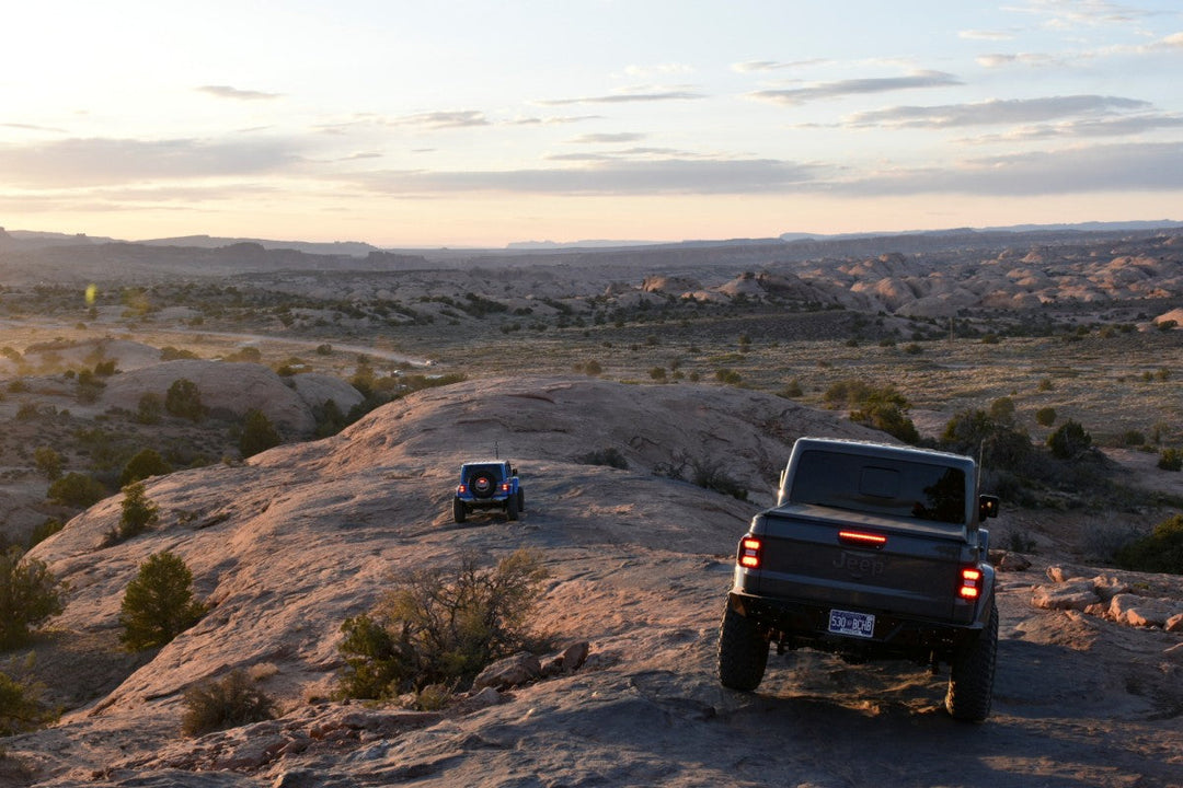 2025 Jeep Wrangler vs the competition comparison with off-road trucks navigating rocky desert terrain at sunset.