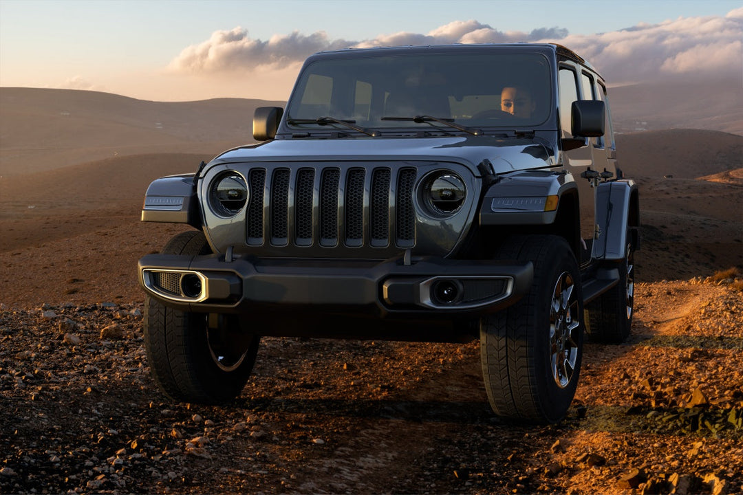 Front three-quarter view of a Jeep Wrangler Sahara off-road at sunset, illustrating the jeep sahara vs wrangler comparison