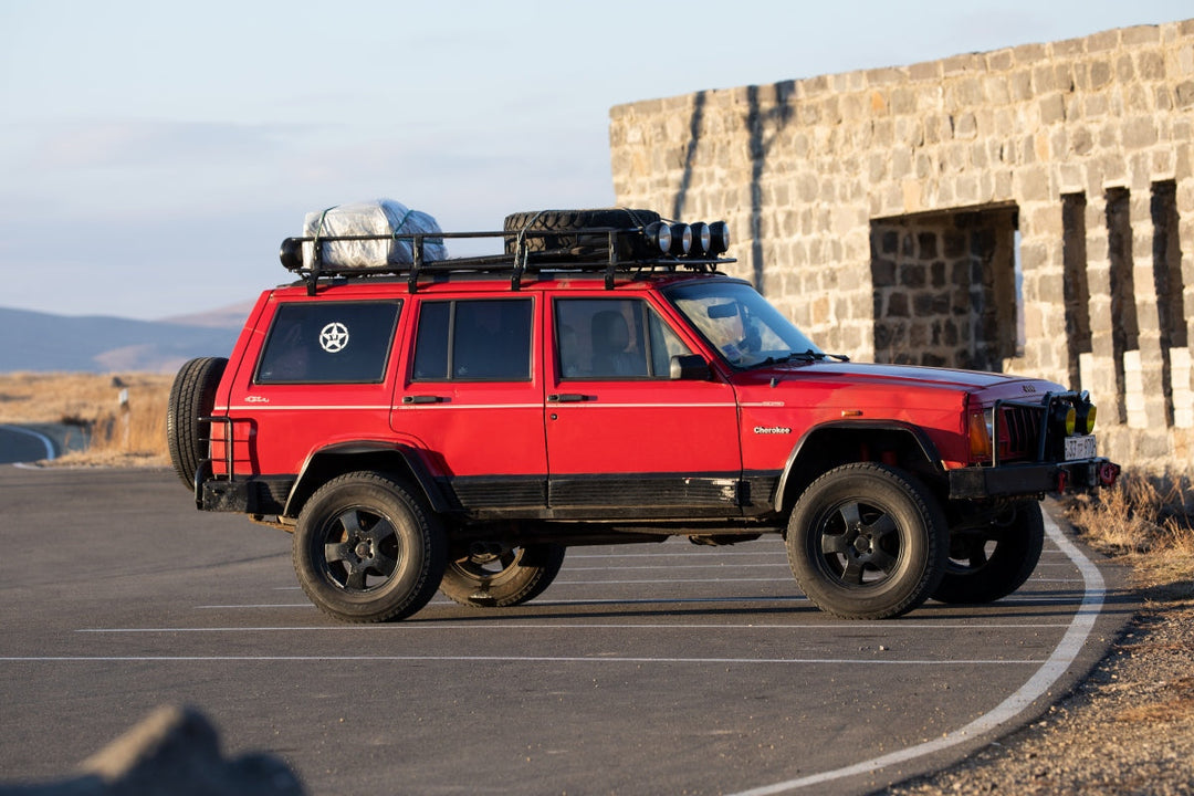 Red Jeep Cherokee XJ with roof rack and spare tire, representative of the best jeep cherokee year for trail-ready builds.